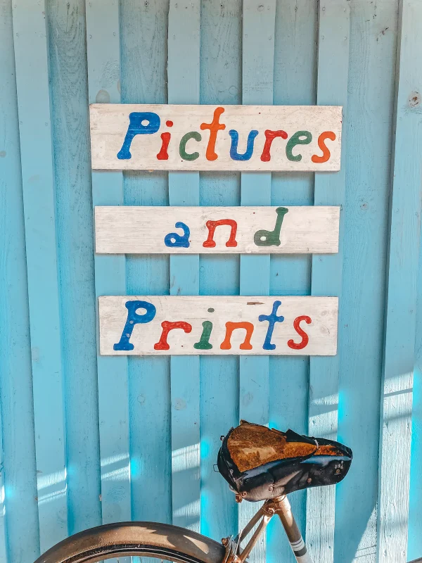 ป้ายร้านไม้เขียนมือคำว่า pictures and prints ตัวอักษรหลากสี