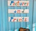 ป้ายร้านไม้เขียนมือคำว่า pictures and prints ตัวอักษรหลากสี