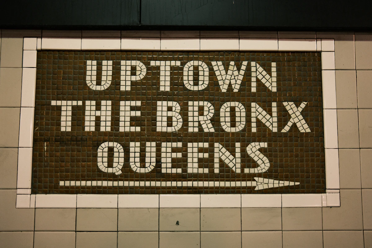 ป้ายบอกทิศ Uptown the Bronx Queens ในรถไฟใต้ดินนิวยอร์ก ตัวอักษรขาวบนดำ